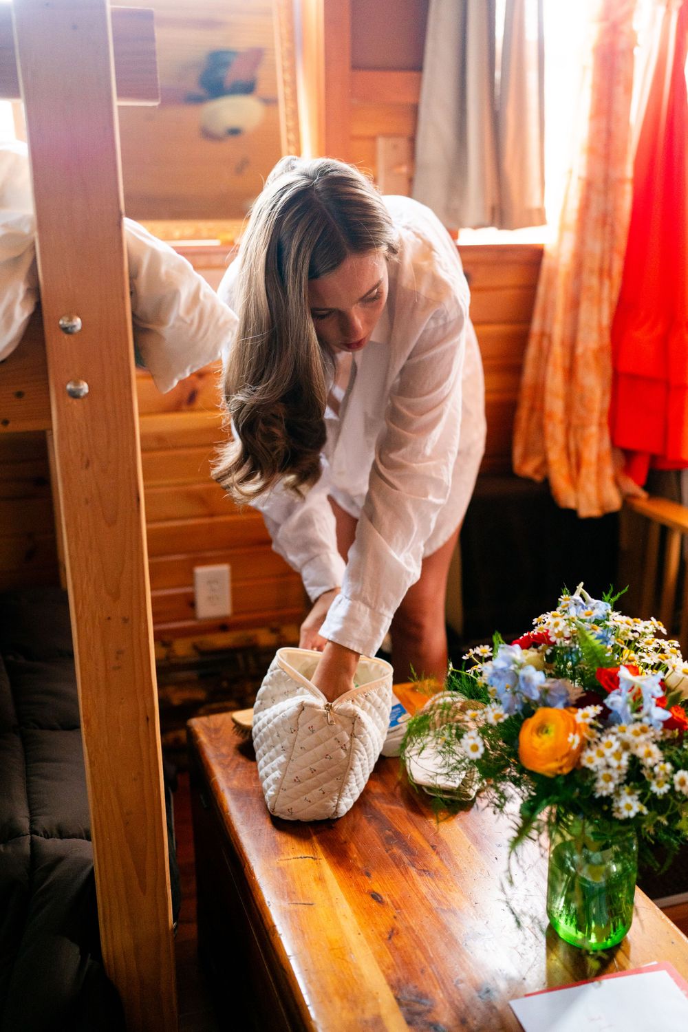 Person in white shirt putting on slippers next to floral arrangement in cabin.