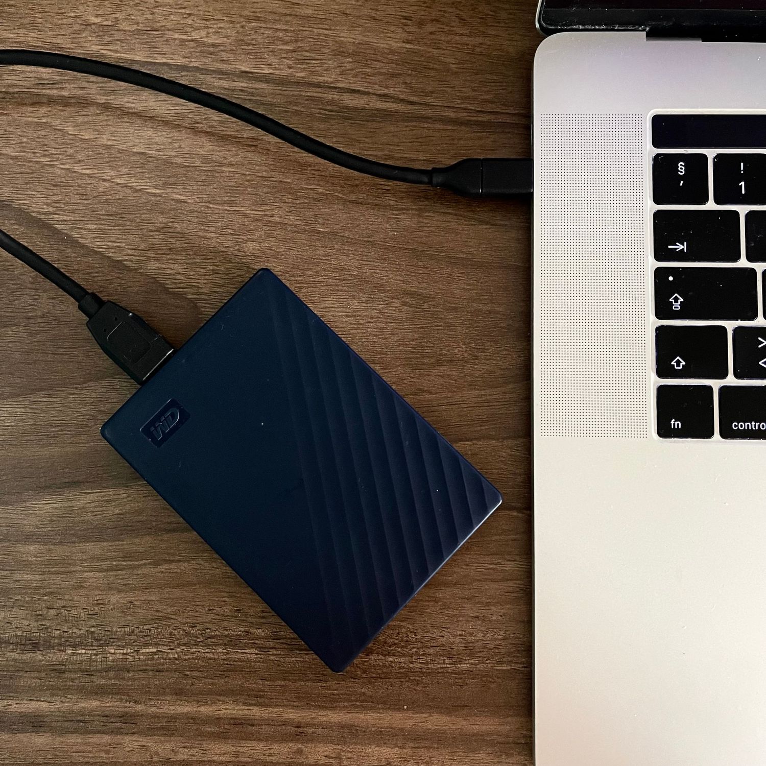 A blue Western Digital portable hard drive connected to a MacBook laptop on wooden surface.
