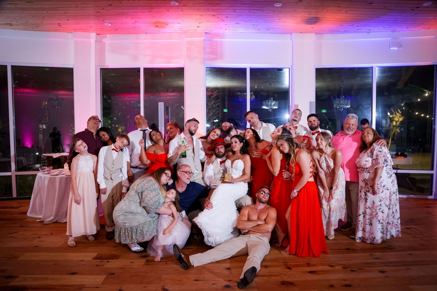 Wedding party poses together under colorful party lights in reception venue.
