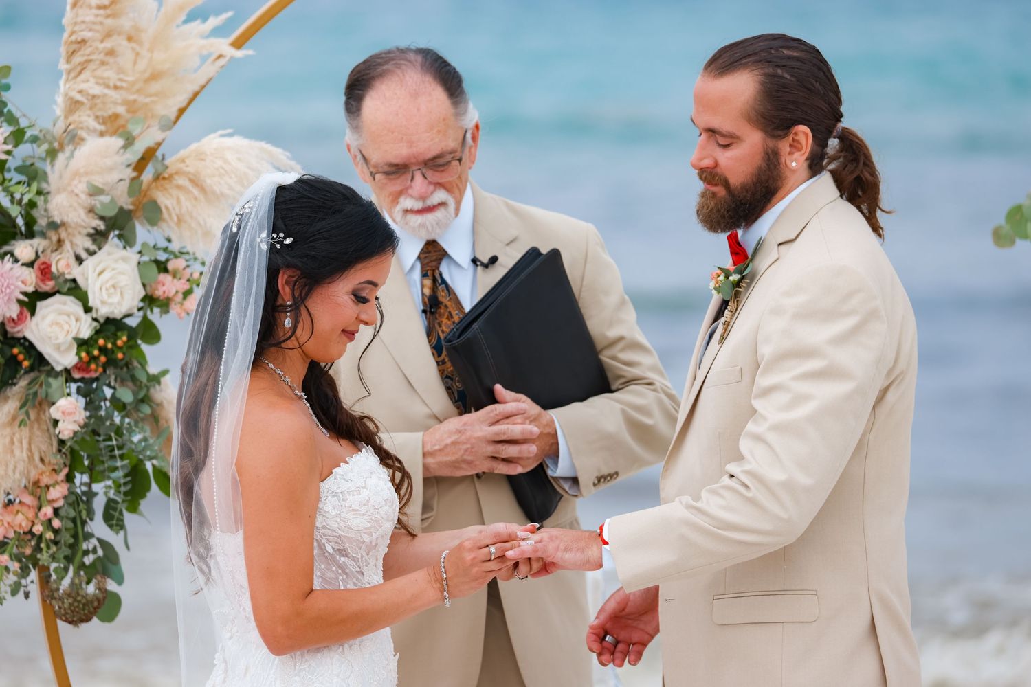 Wedding ceremony in progress under floral arch with ocean waves in background.