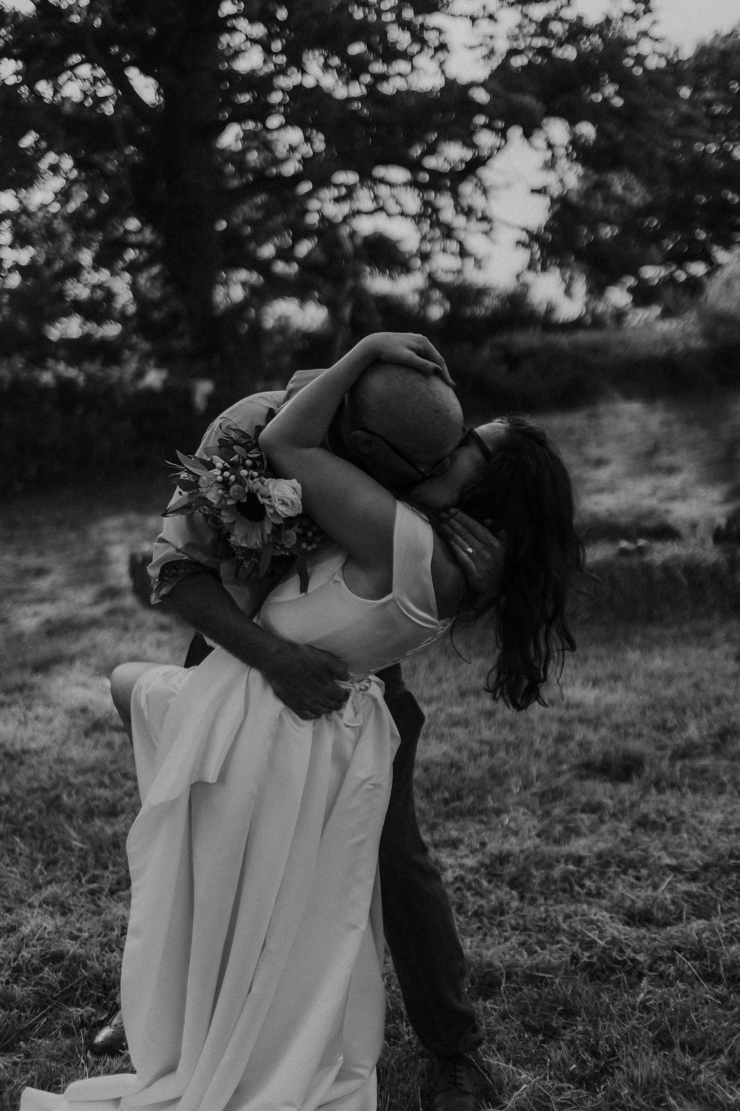 Black and white romantic dip kiss between newlyweds in outdoor setting.