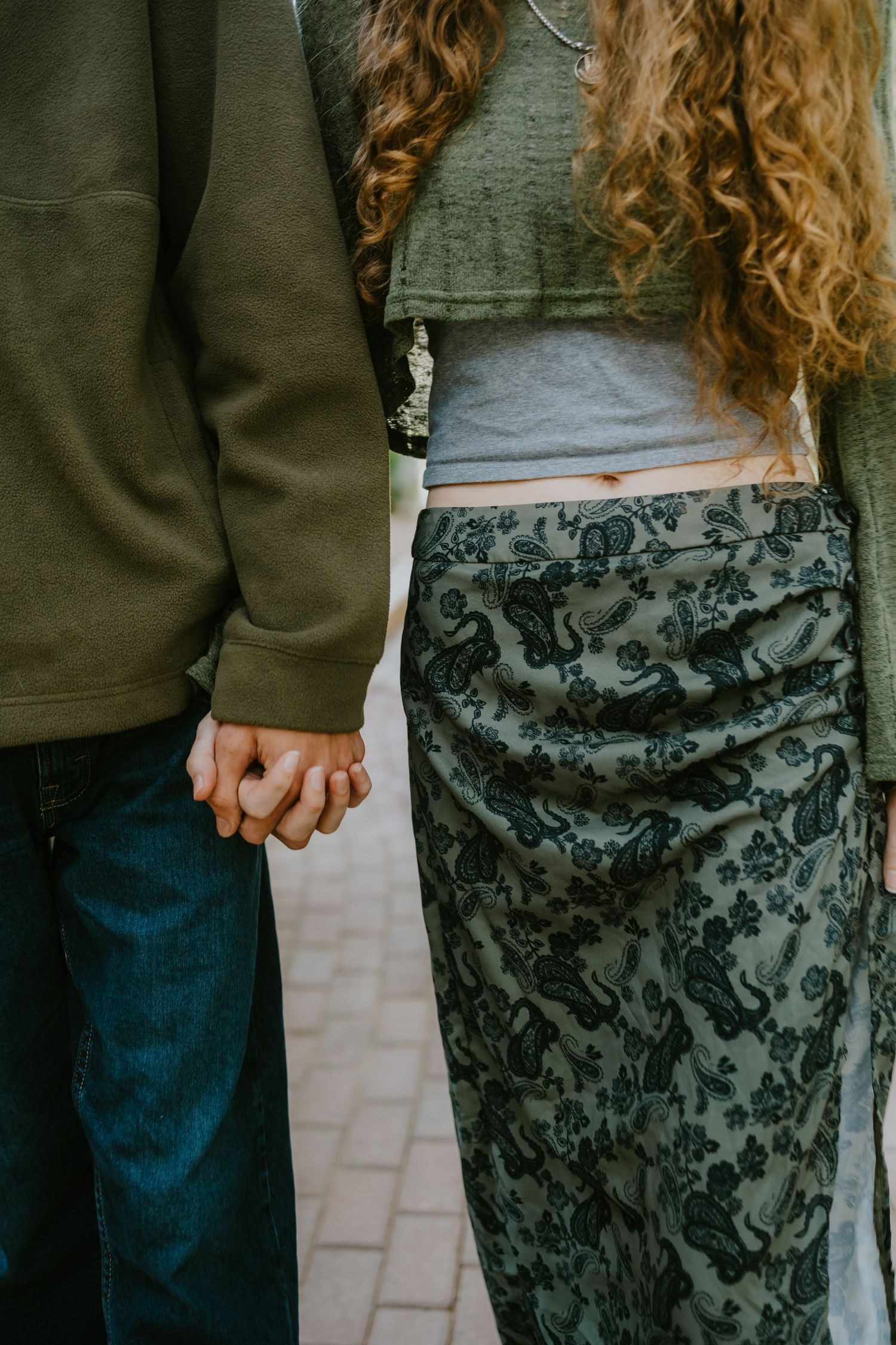 Close-up of couple holding hands wearing casual clothing and floral skirt.