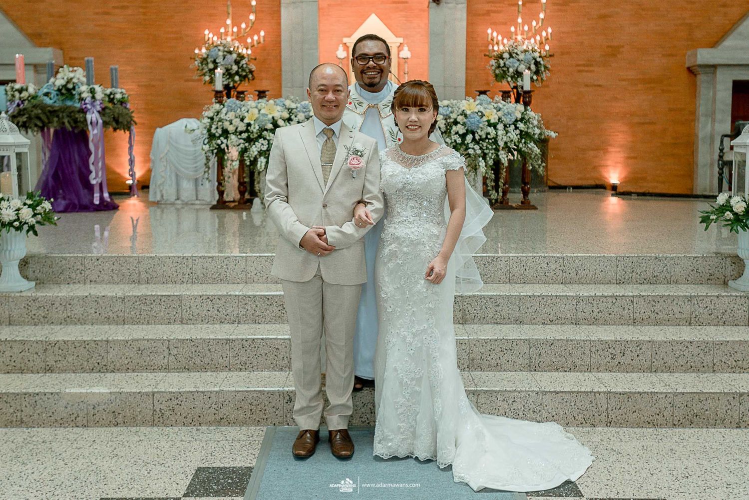 Wedding portrait on stairs with orange walls and elegant white floral arrangements.