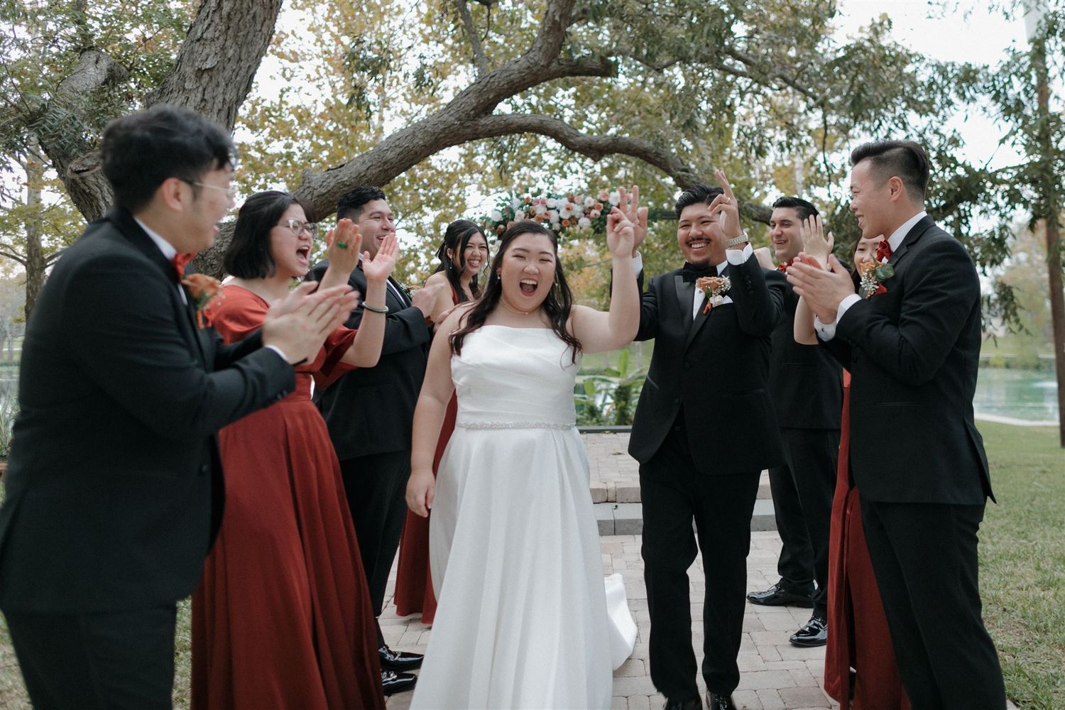 Wedding party celebrates with raised hands during outdoor ceremony.