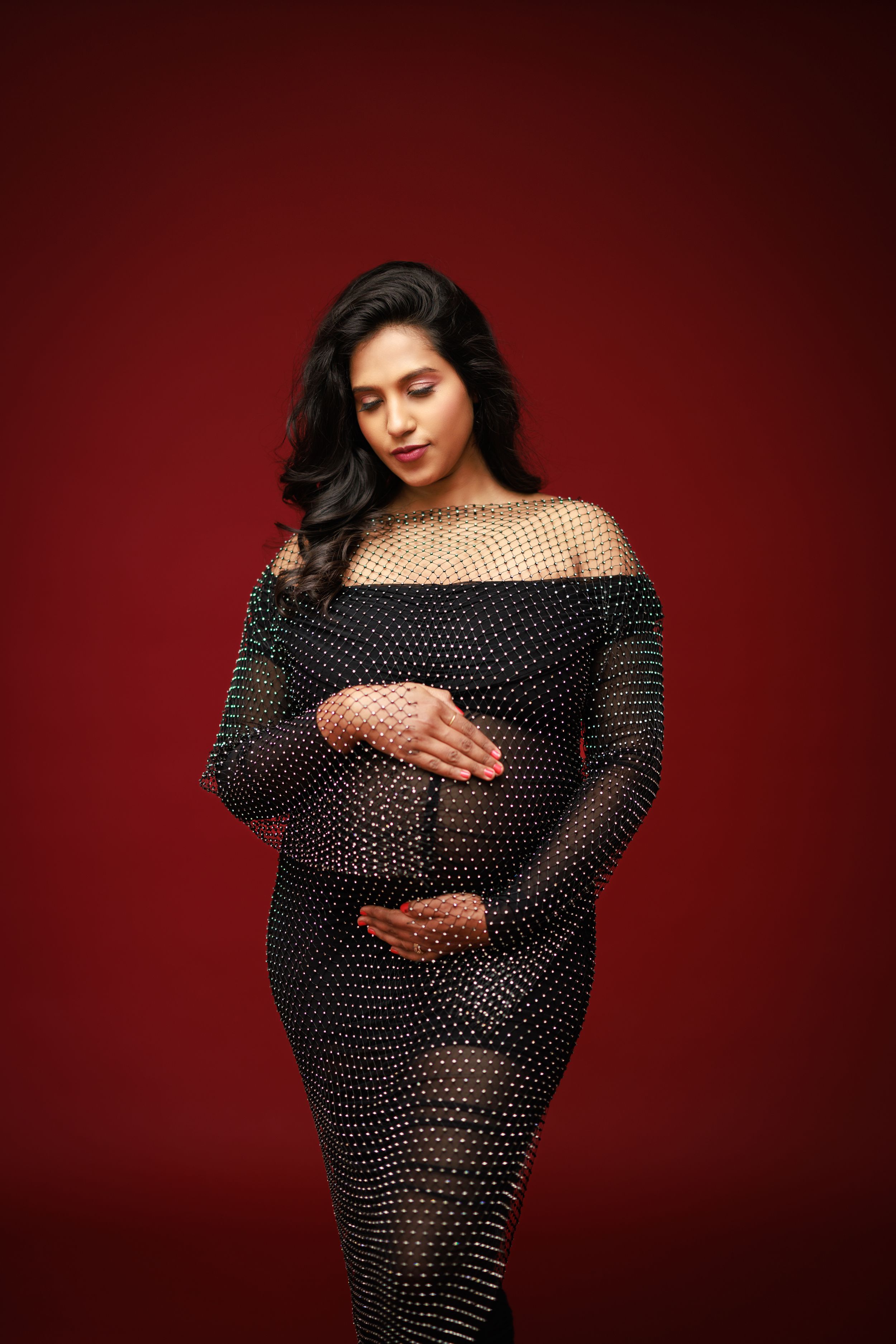 Maternity photo in sheer polka dot dress against deep red background.