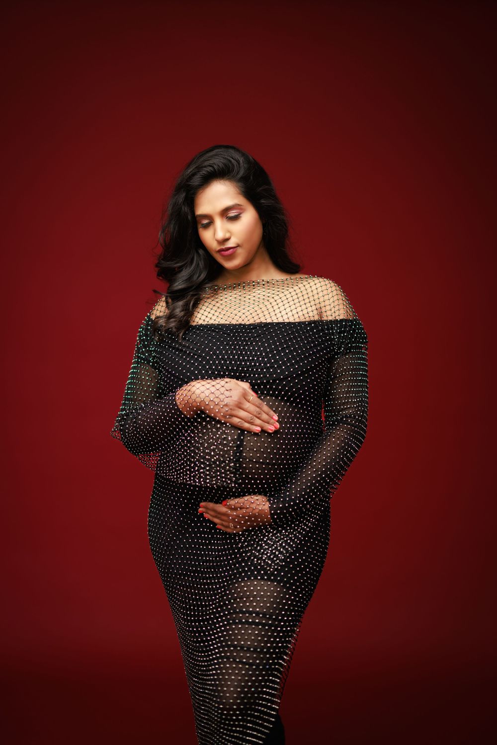 Maternity photo in sheer polka dot dress against deep red background.