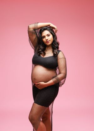 Maternity portrait in black mesh dress against pink background.