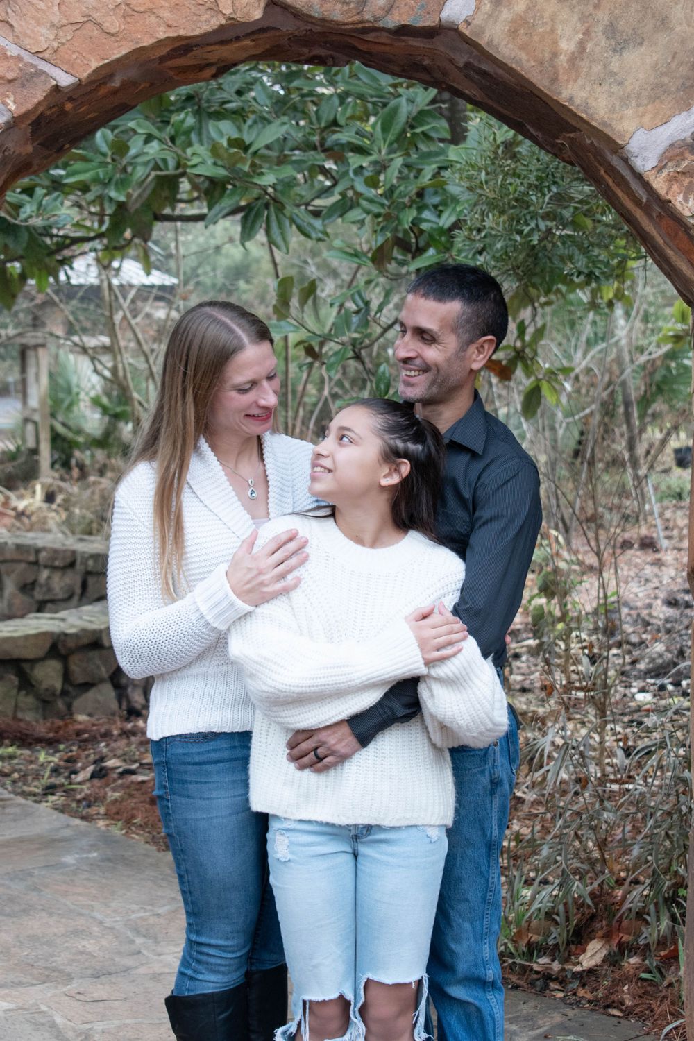 Family sharing an intimate moment together while posing under a stone archway with greenery.