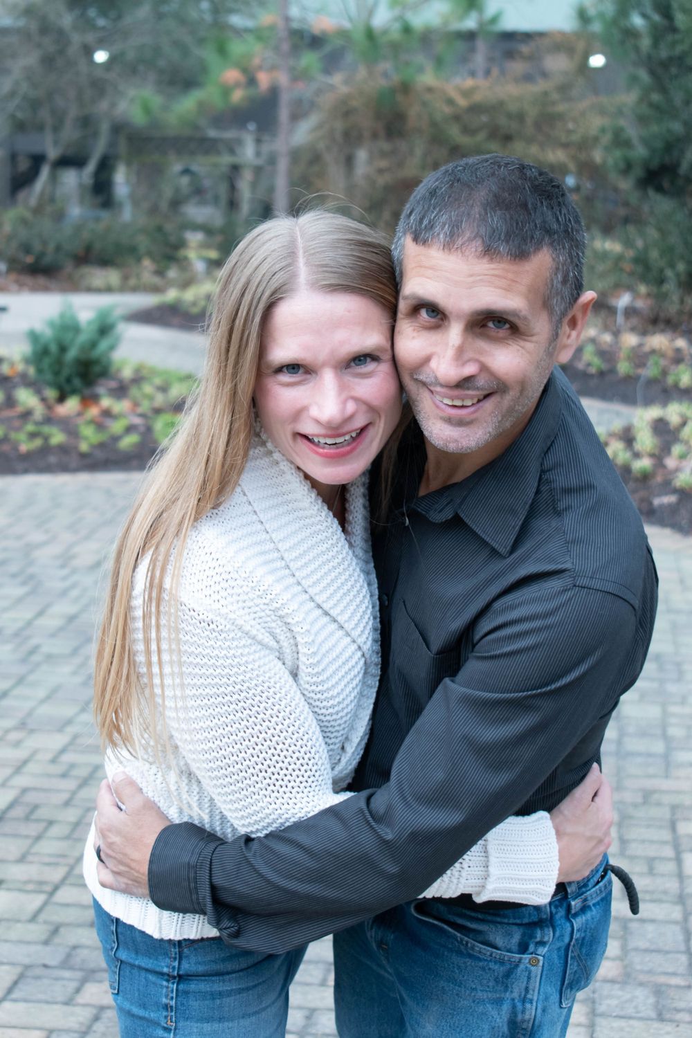 Couple embracing and smiling outdoors on stone pathway.
