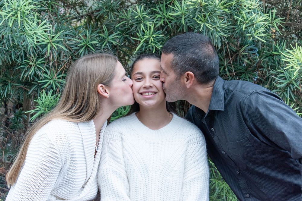 Affectionate family moment captured outdoors against green foliage.
