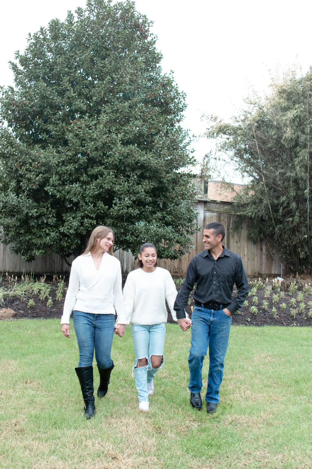 Family walking together holding hands on a grassy lawn with trees in background.