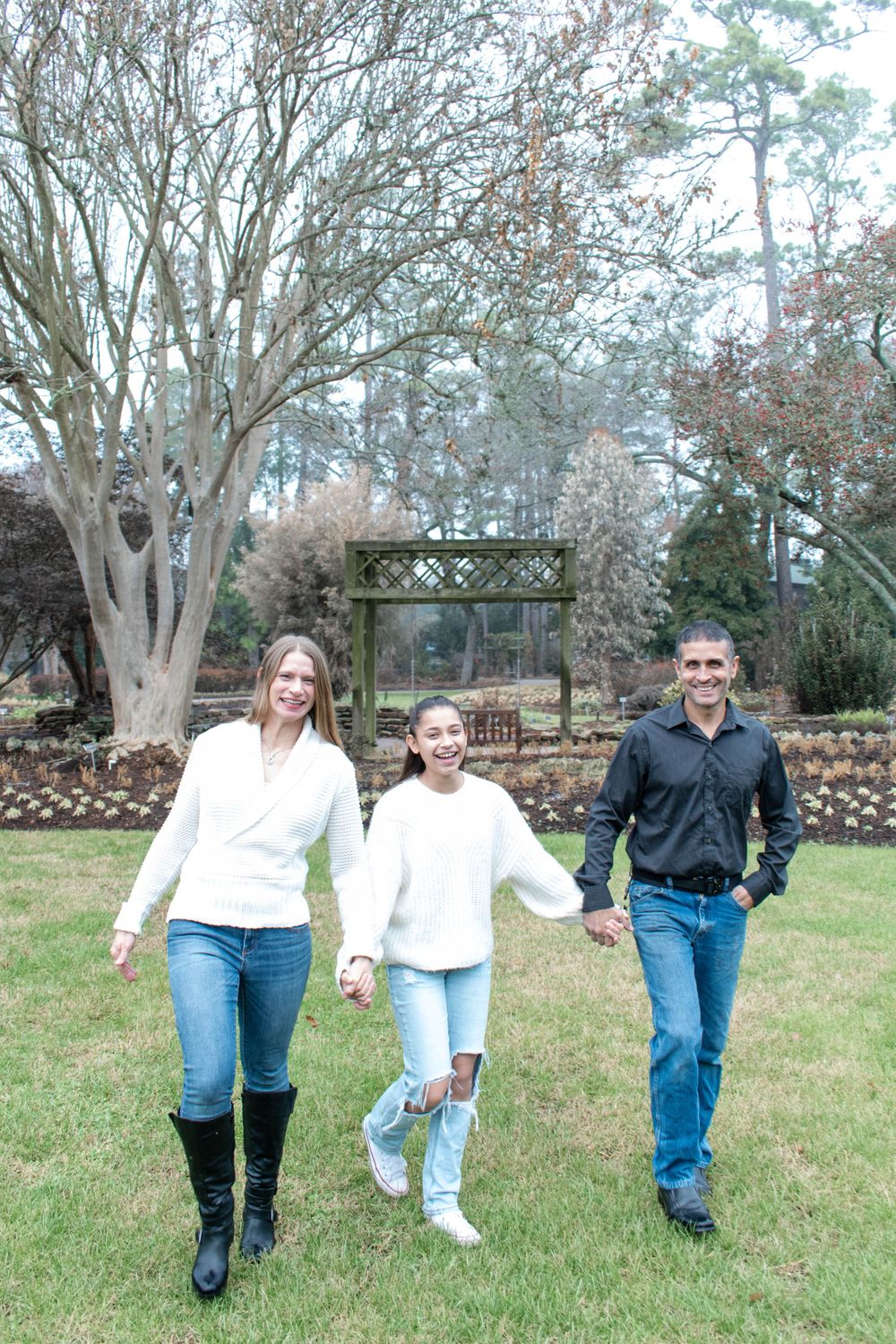 Family walking together on grass with wooden garden arch in background.