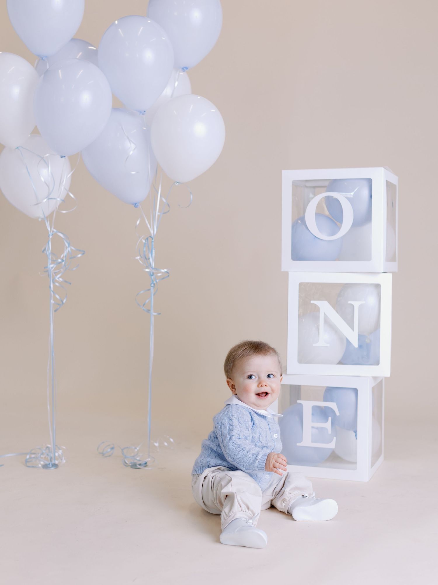 Baby sitting next to white ONE blocks and balloons in studio setting.