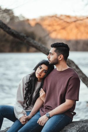 Romantic couple sitting on rocks by the water during golden hour.