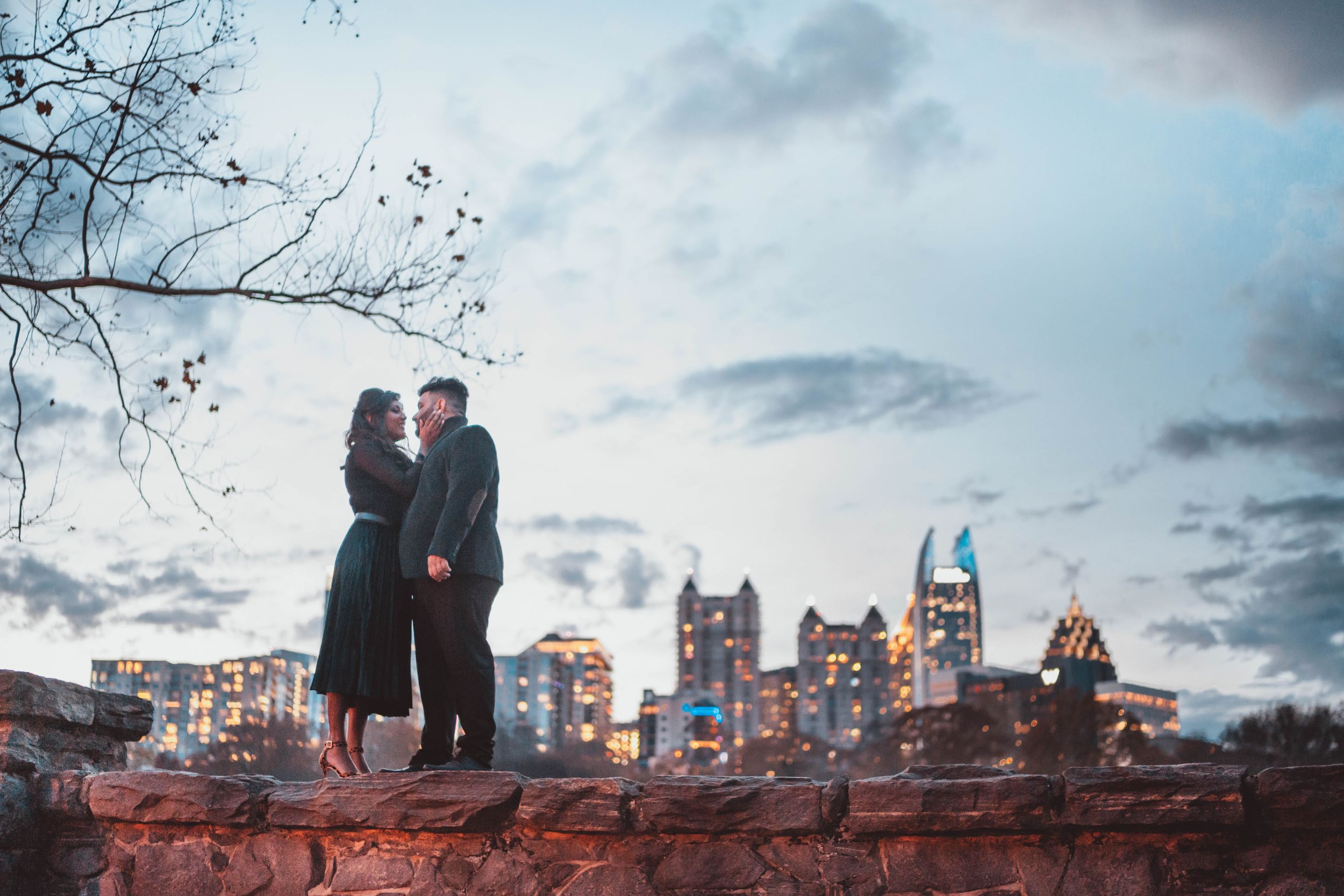 Silhouette of a couple against a dramatic evening sky with city buildings in the background. Atlanta skyline