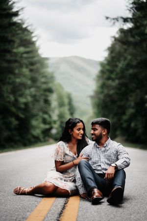 Couple lounging on mountain road during intimate photoshoot session.