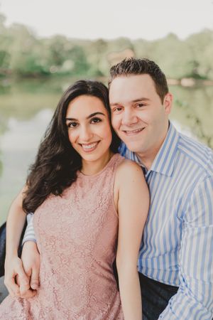 Engagement photo of a couple in pink dress and striped shirt posing outdoors.