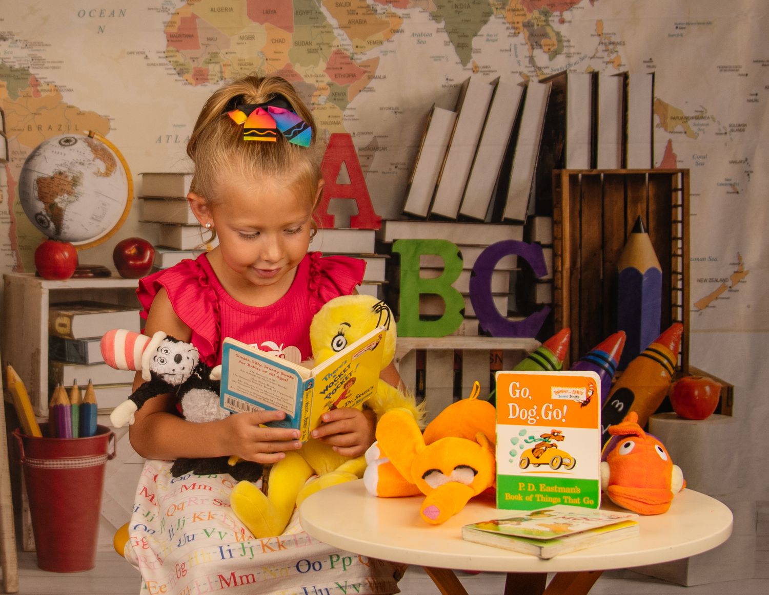 Child reading with stuffed animals at desk with world map and educational materials in background.