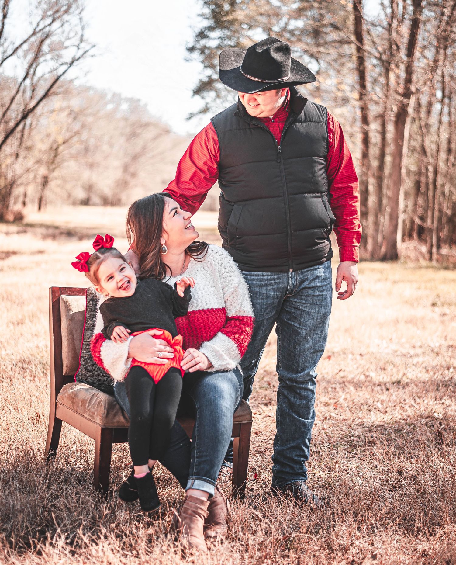 Happy family with toddler in red bow poses outdoors in winter field setting.