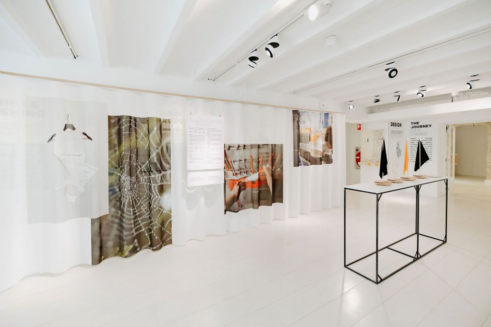 Contemporary exhibition space with abstract artwork hanging on white walls and black display stands.