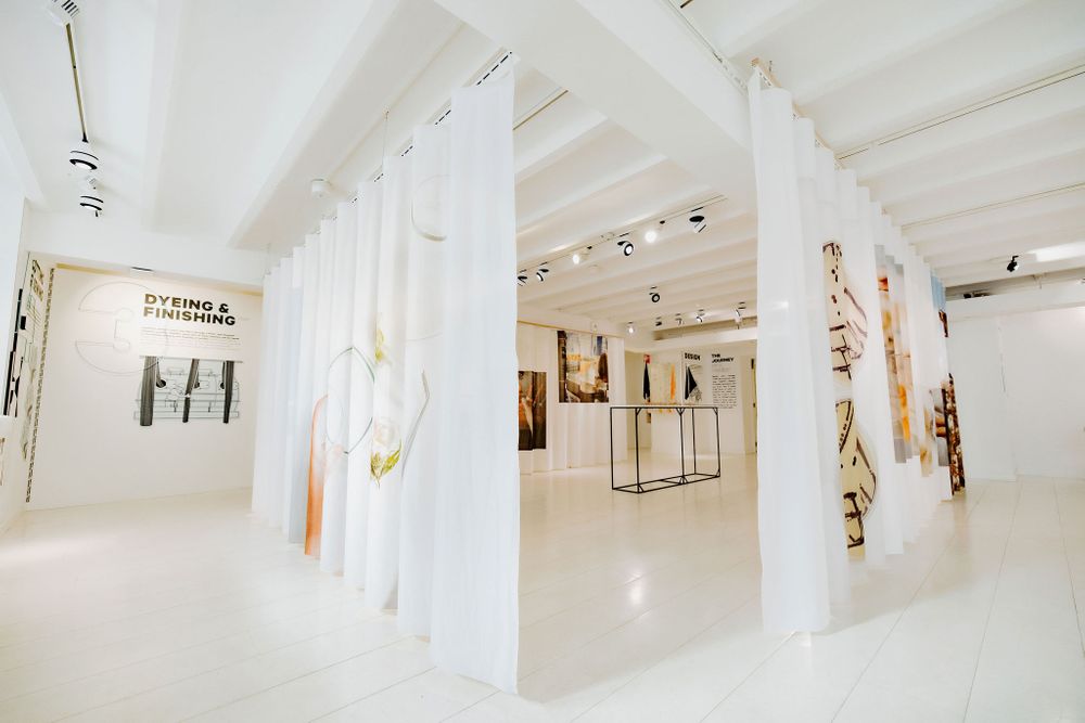 White gallery space with hanging fabric panels and art installations creating geometric pathways.