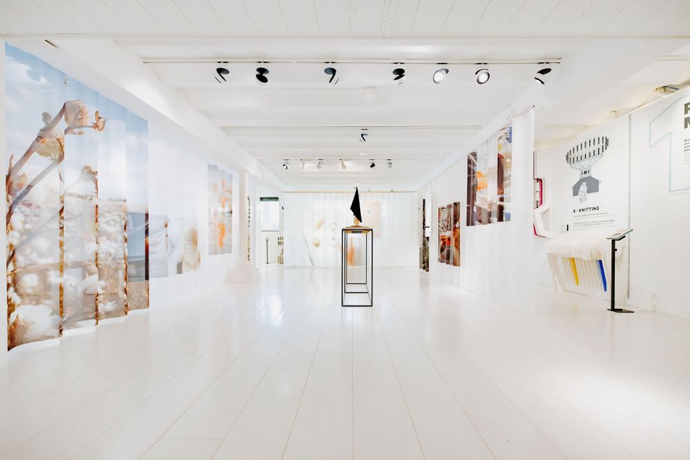 Spacious gallery with high ceilings displaying mixed media artwork and freestanding display cases.