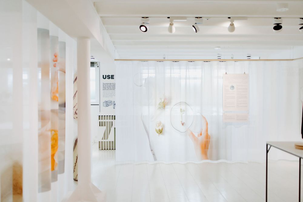 Modern art gallery interior with white walls and sheer fabric displays illuminated by track lighting.