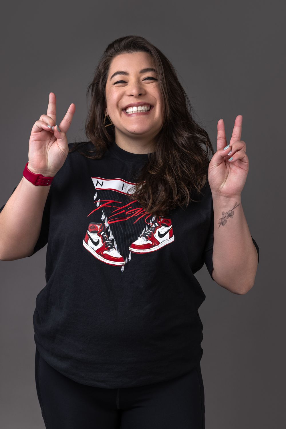 Smiling woman in Jordan sneaker graphic tee making peace signs against gray background.