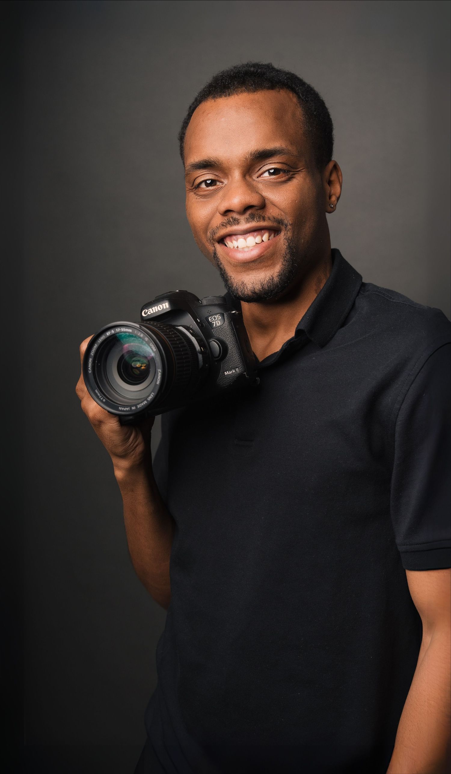 Professional photographer holding DSLR camera against dark background.