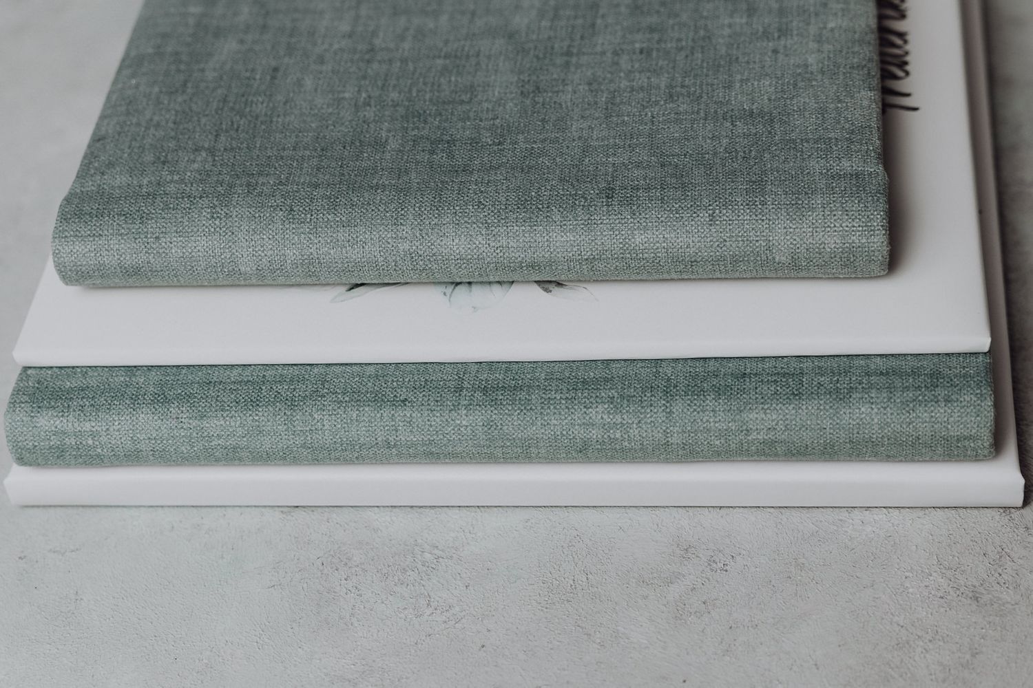 Stack of gray and white linen-bound photo albums on light concrete surface.
