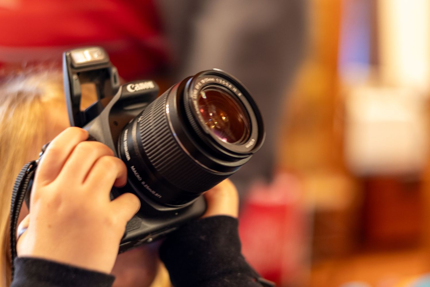 Close-up shot of hands holding a DSLR camera with a telephoto lens.