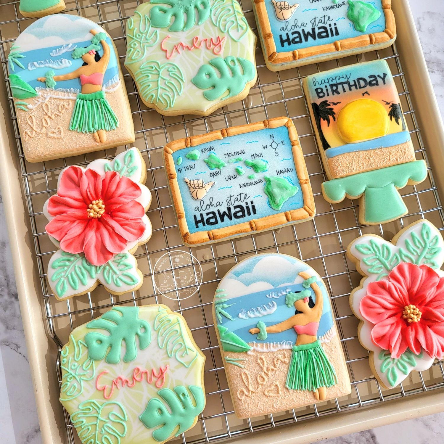 Overhead view of a tray of decorated sugar cookies with a tropical Hawaii theme, including hula dancers, hibiscus flower and beach scenes.