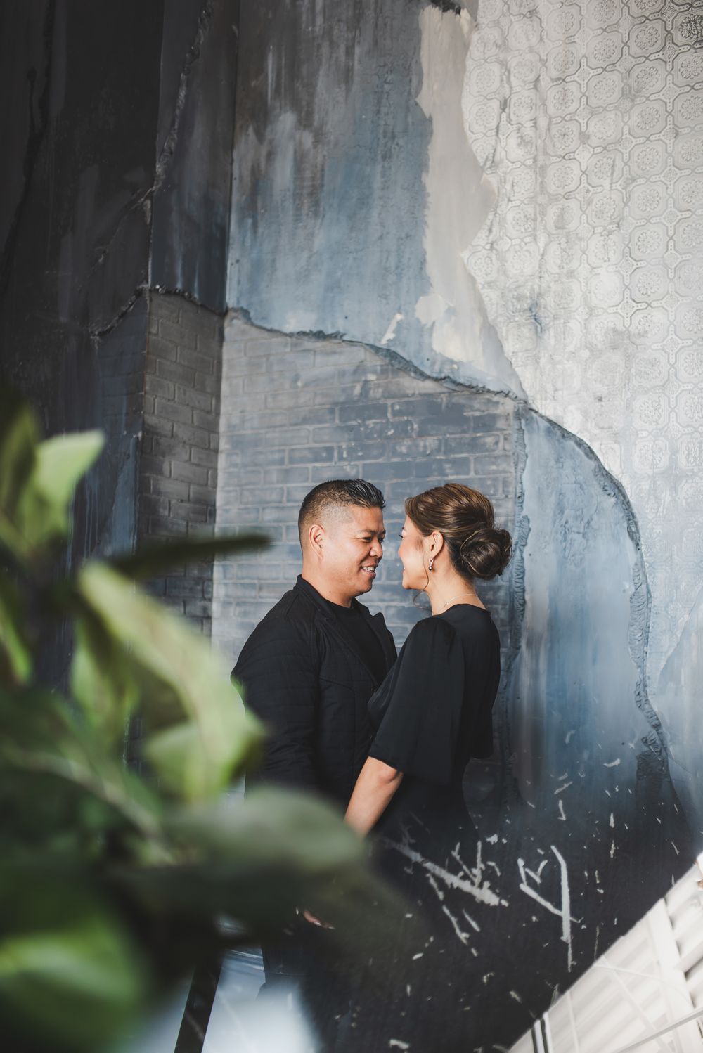 A couple shares an intimate moment against a textured blue and grey wall.