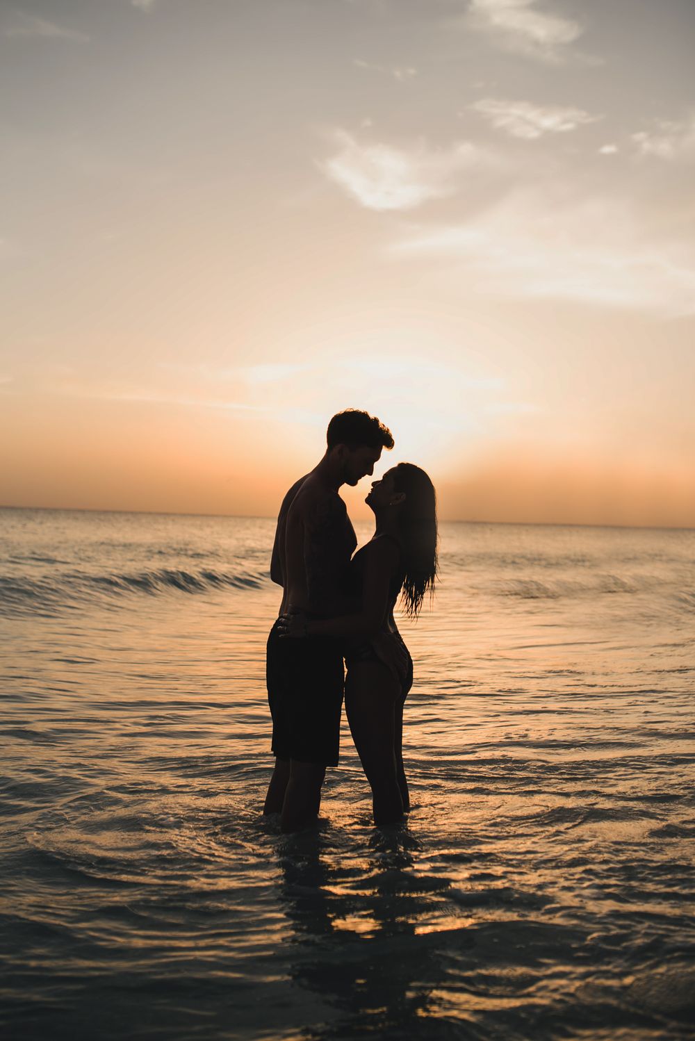 Silhouette of a couple standing in ocean water during sunset.
