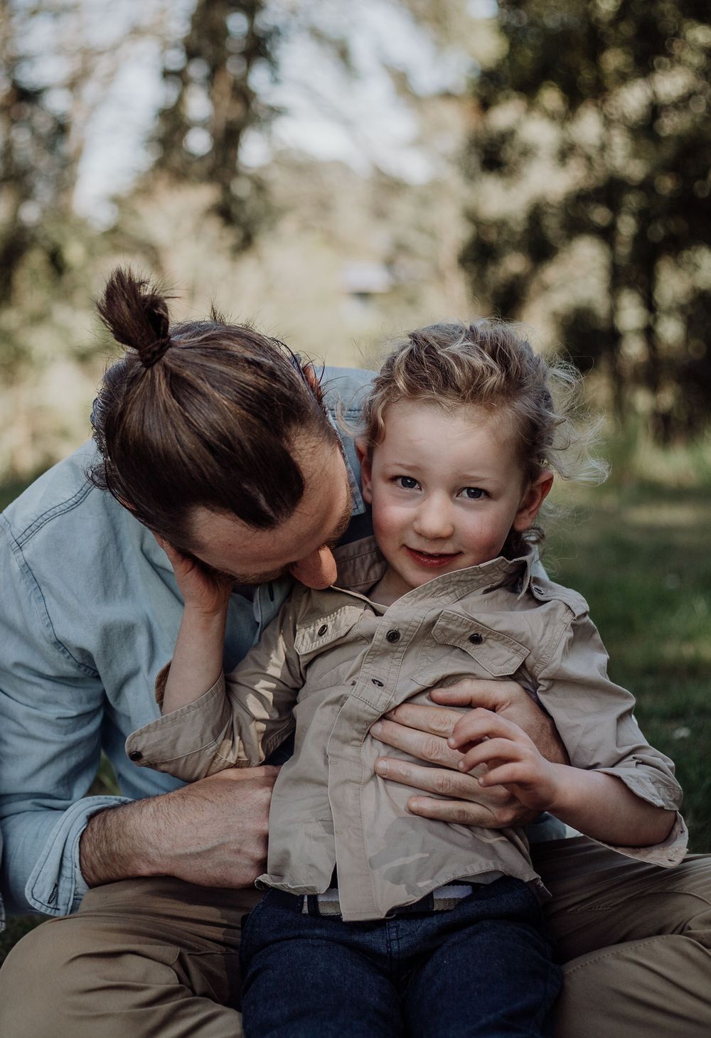 Two figures share an intimate moment of joy while sitting together outdoors in natural lighting.