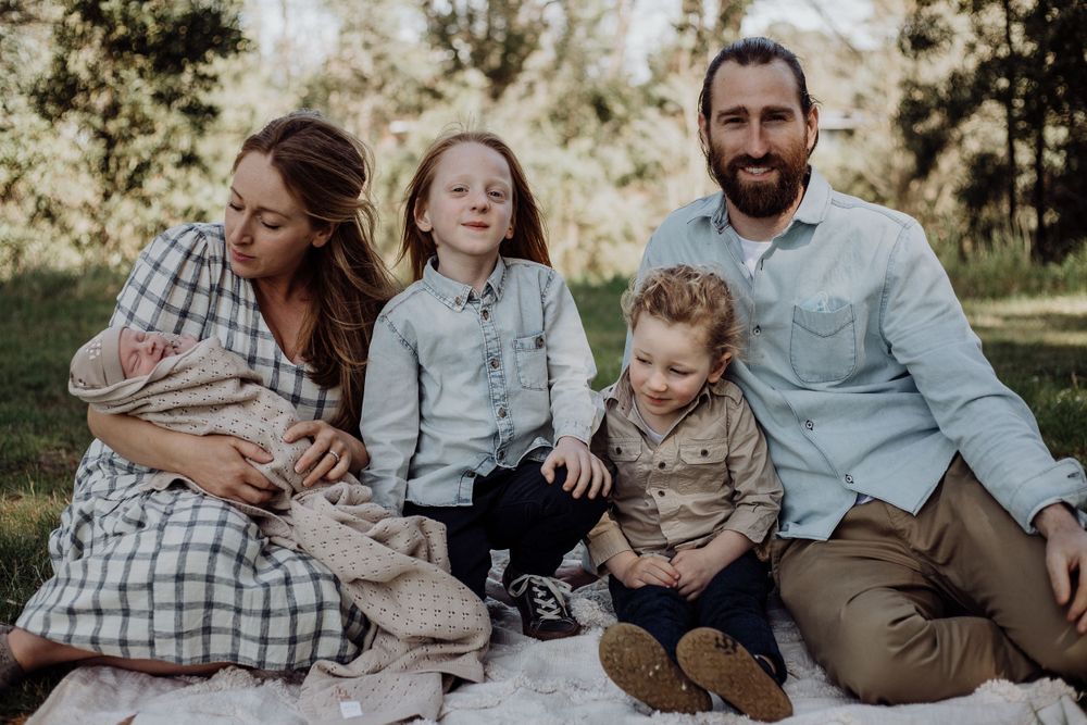 A family group sits casually together on a white blanket for an outdoor portrait.