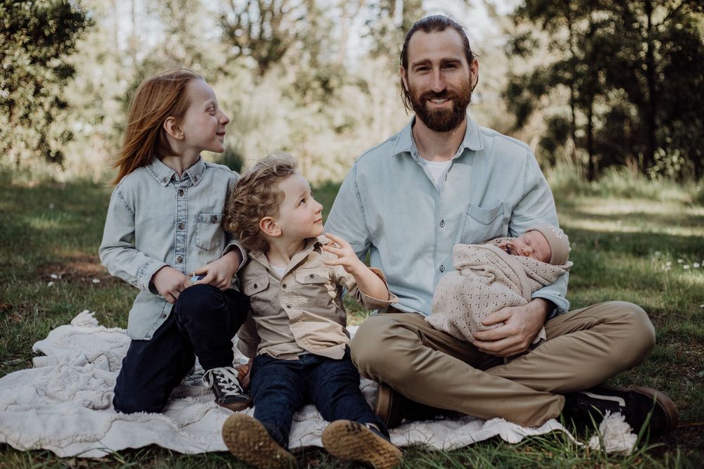 A family group sits together on a light blanket during an outdoor photo session.
