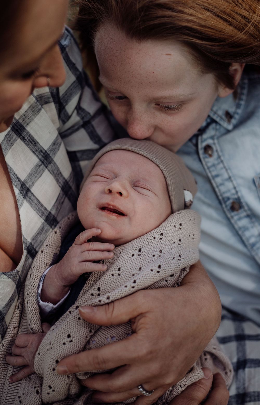 An intimate close-up of two people gazing lovingly at a newborn wrapped in a speckled blanket.