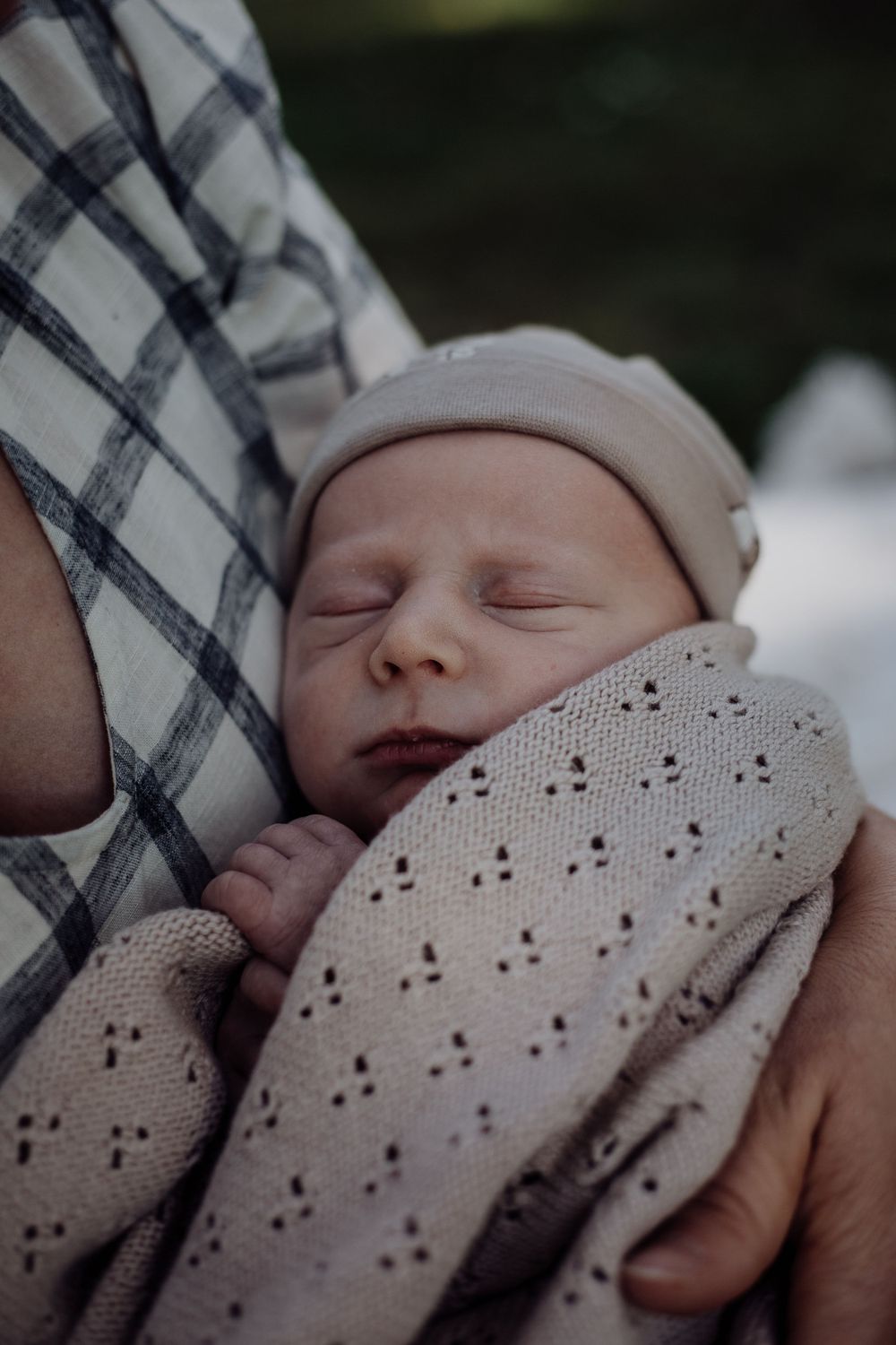 Close-up of a sleeping newborn baby wearing a beanie and wrapped in a dotted blanket.