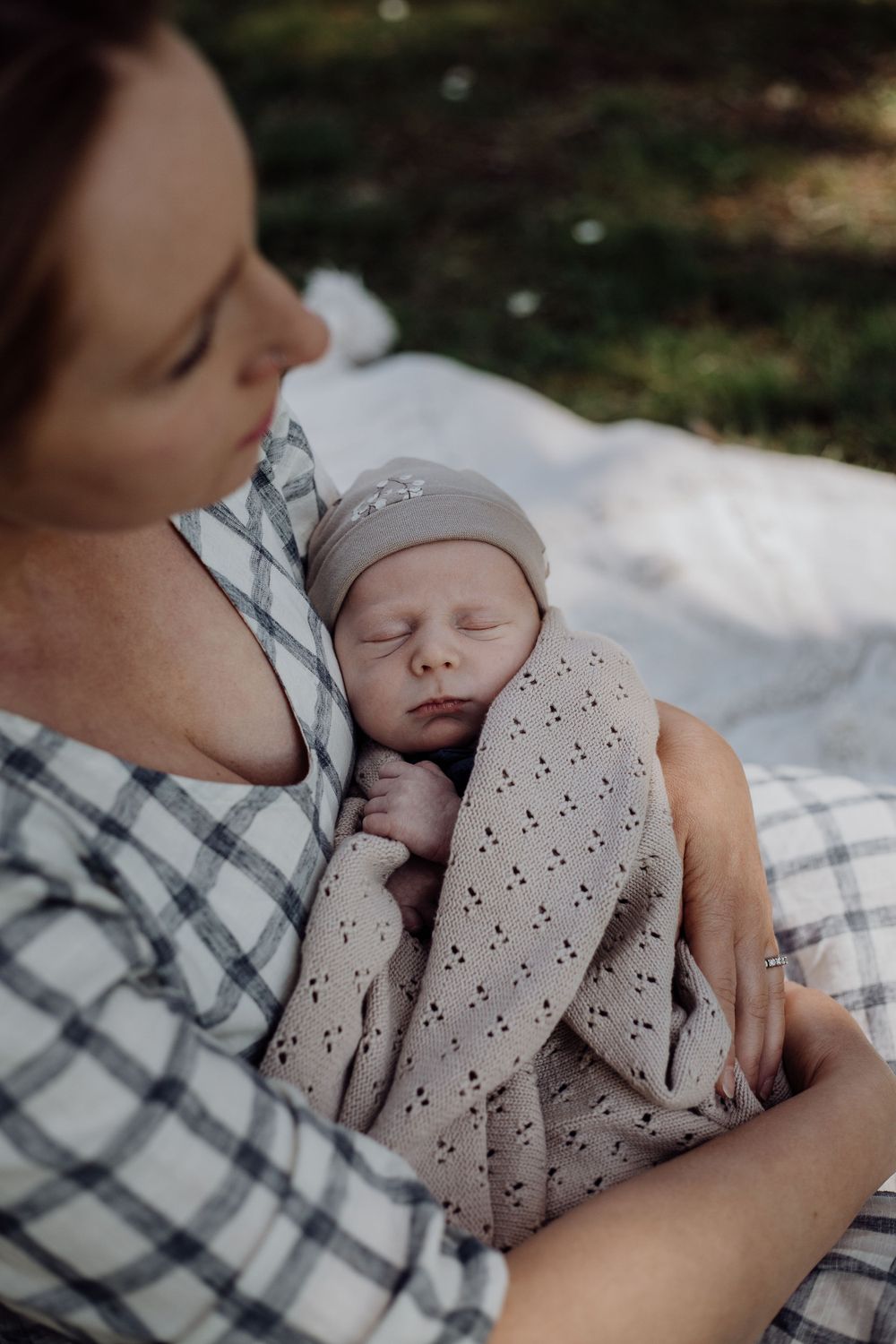 A mother in plaid holds her sleeping newborn close in a polka dot blanket.