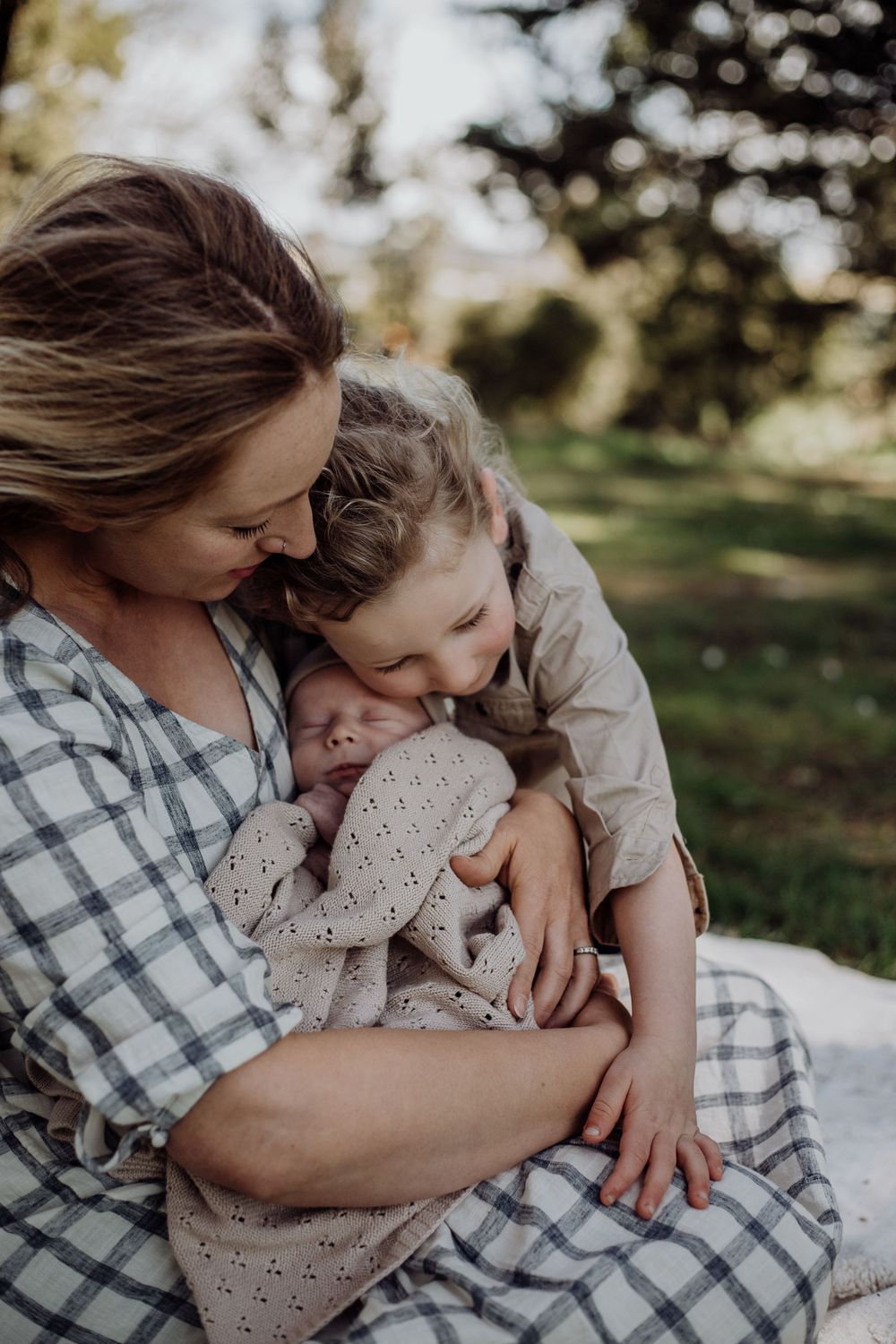 A tender family moment as siblings bond with their new baby outdoors.