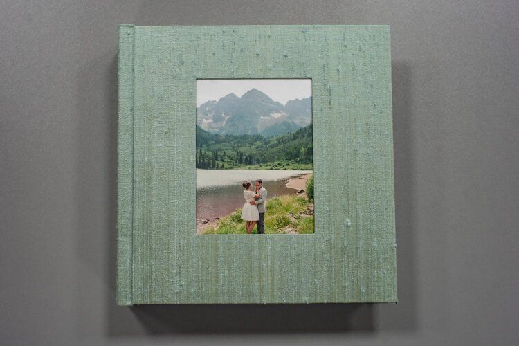 A mint green wedding album with a small photo window displaying a mountain landscape.