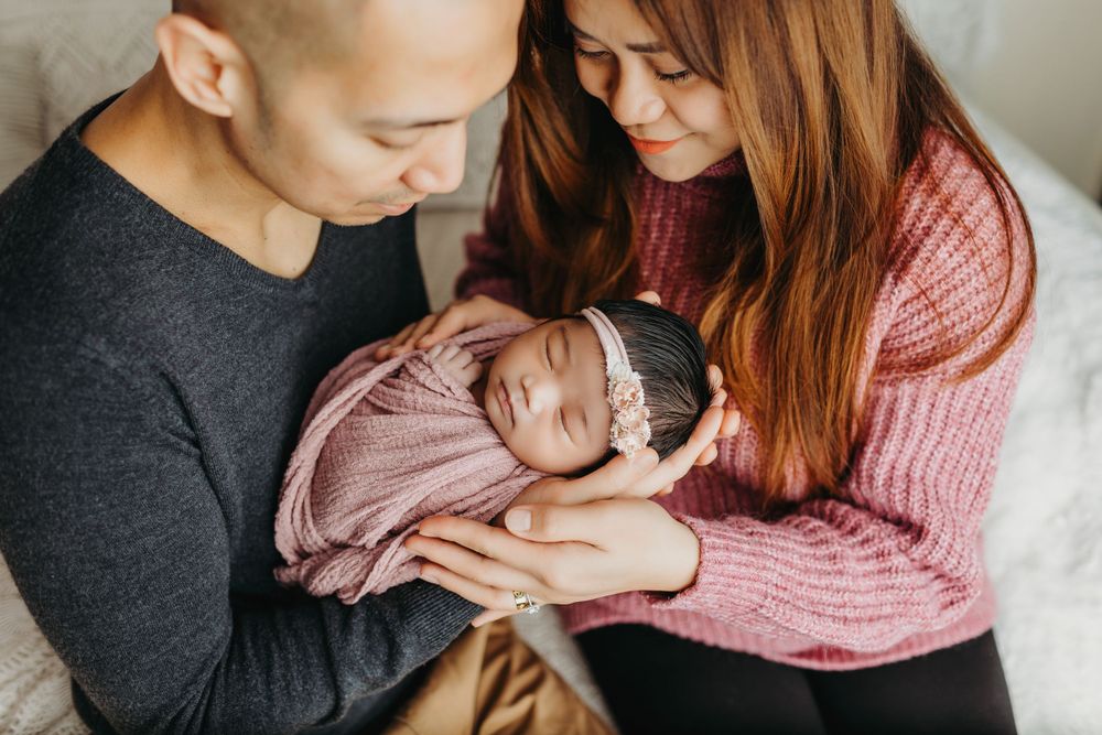 Parents in casual wear holding and looking lovingly at their newborn.
