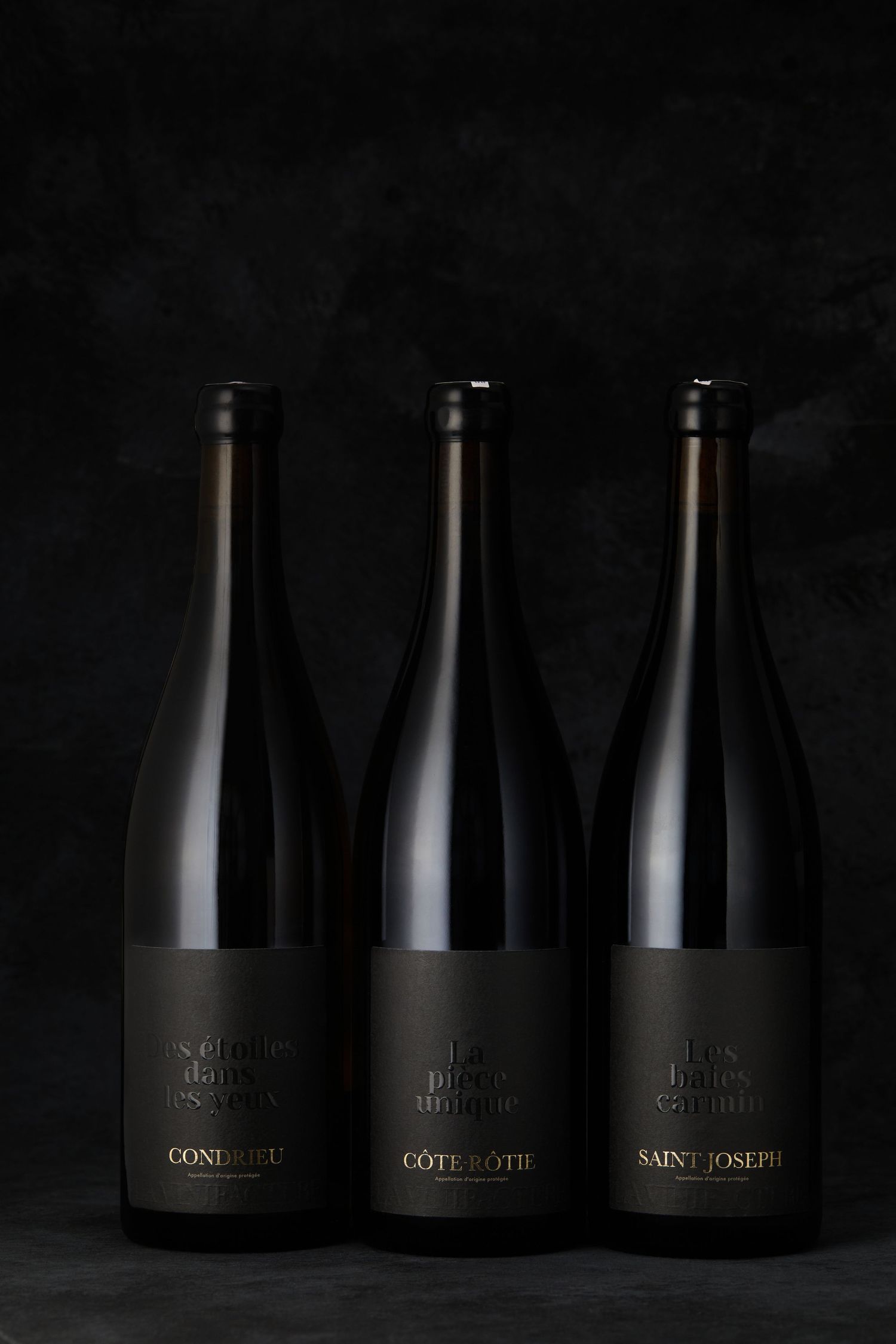 Three dark wine bottles with minimal black labels against dark background.