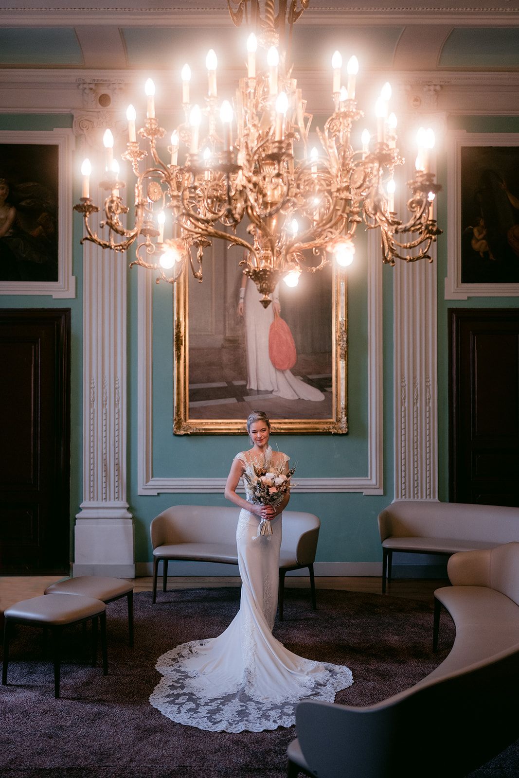 Elegante trouwjurk tentoongesteld in luxe kamer met grote kroonluchter en turquoise muren in Sint-Truiden