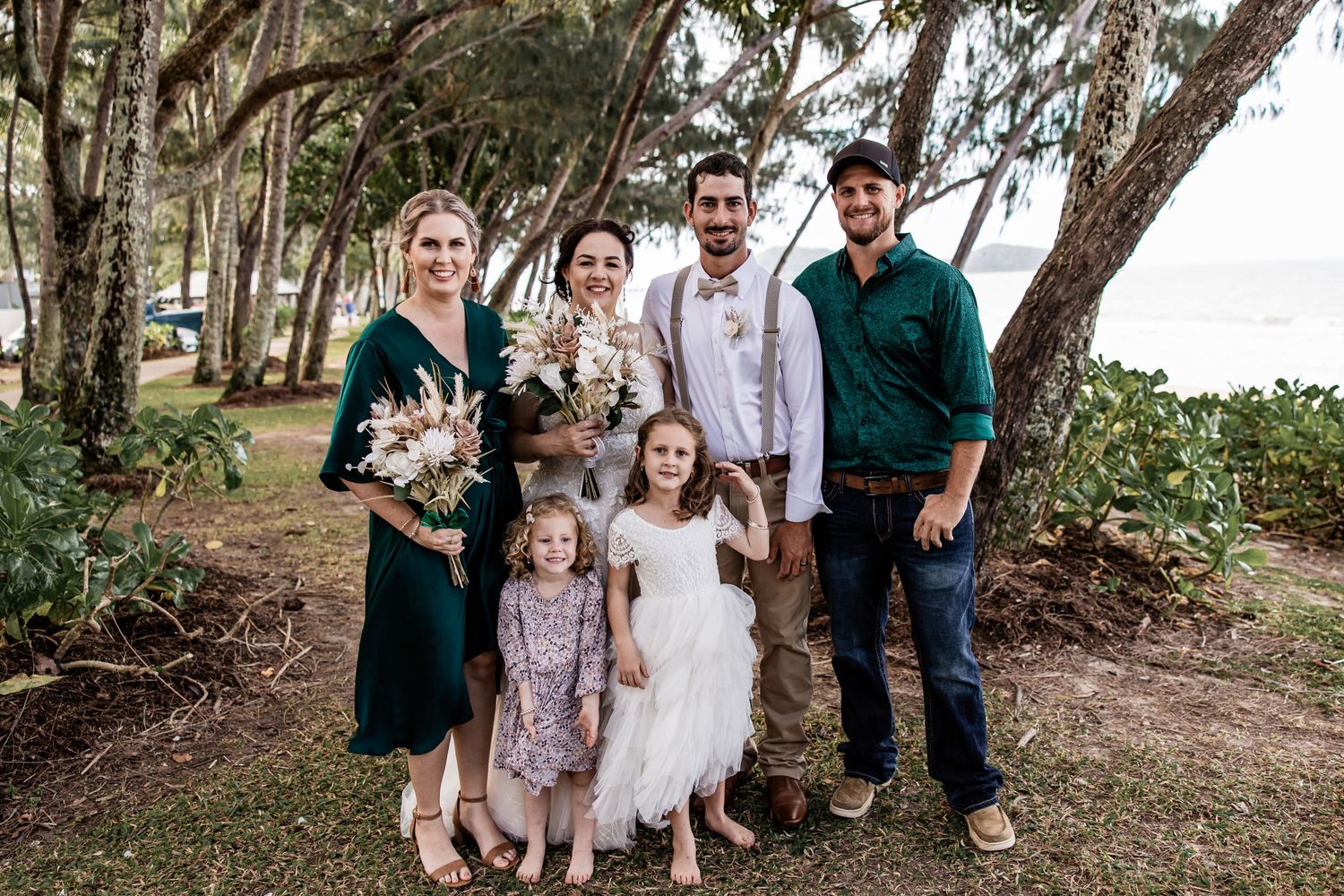 A small family group poses together under coastal trees near the beach.
