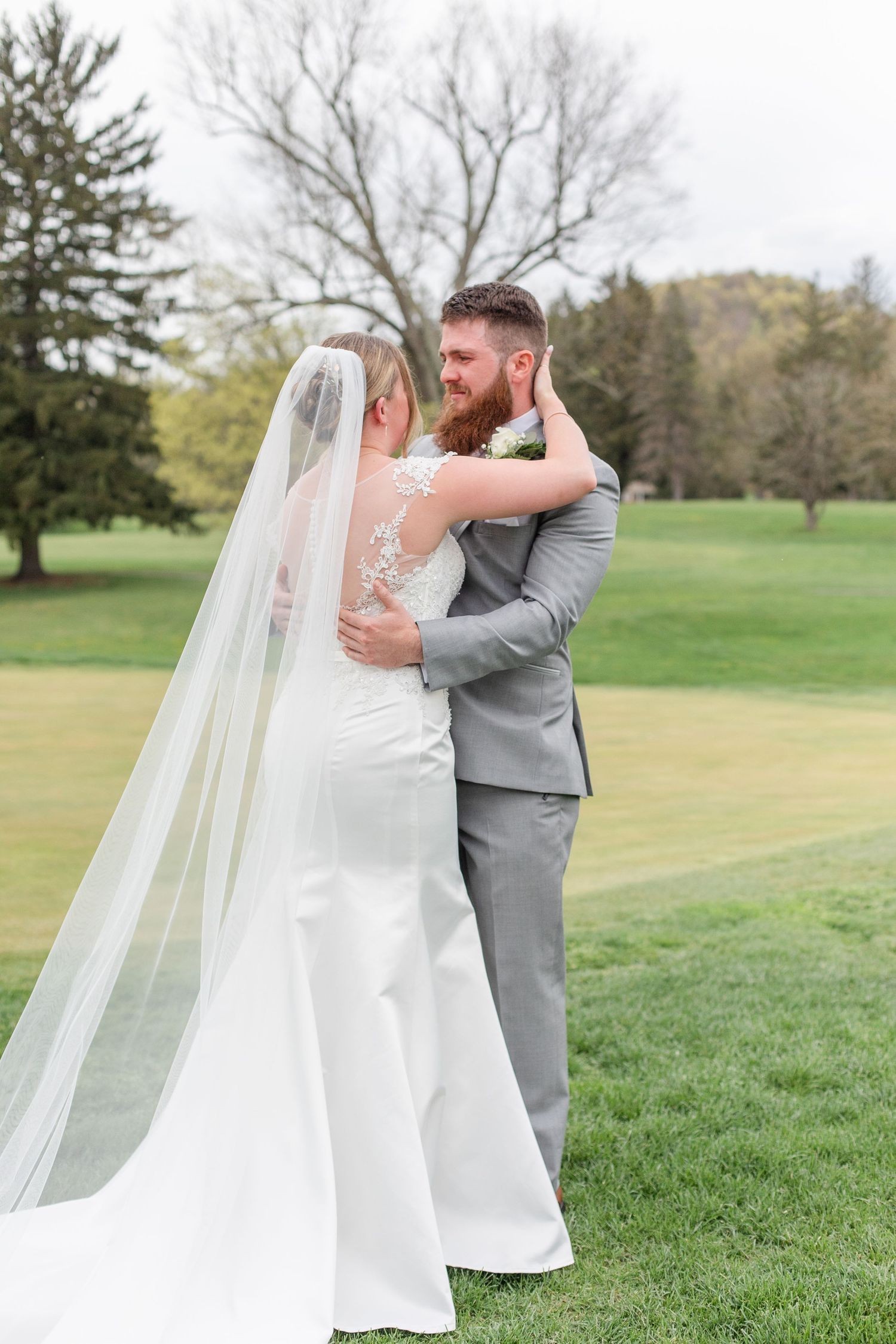 A romantic wedding moment captured on a golf course with flowing white veil and gray suit.