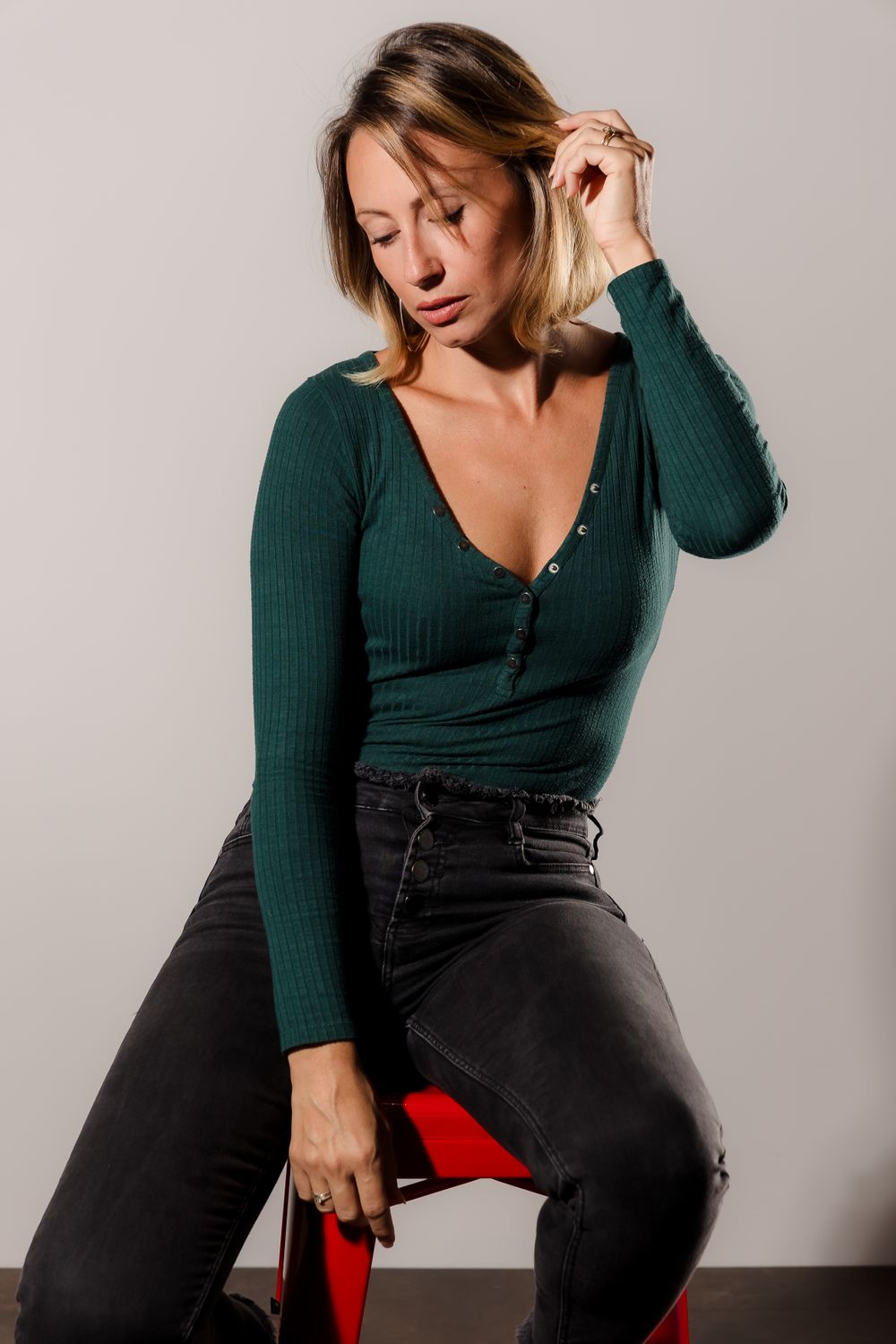 Portrait series of someone wearing green top and dark jeans while posing on red chair.