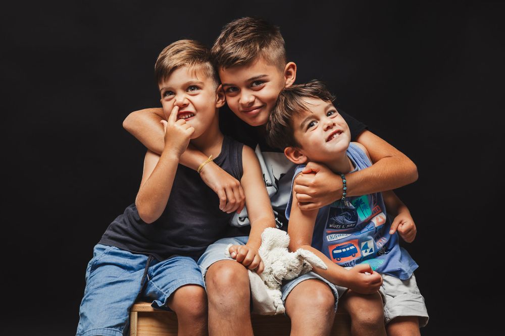 Group of children in casual wear posing playfully together on brown couch.