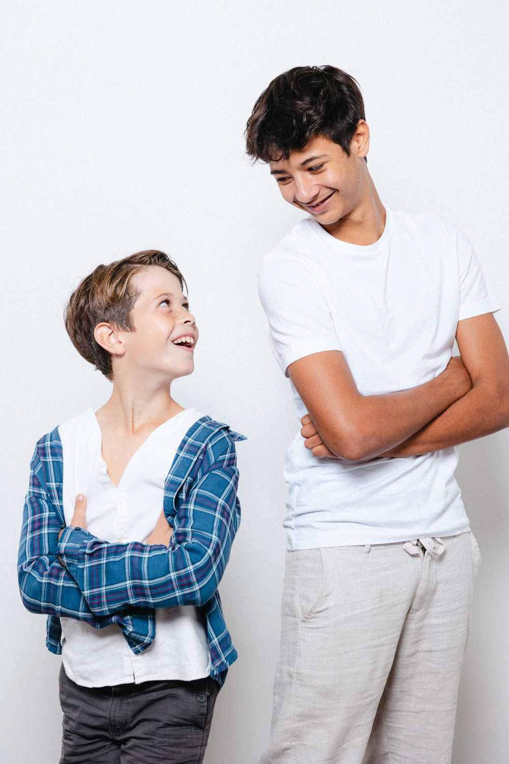 Two people in casual clothing share a candid laughing moment against a white background.